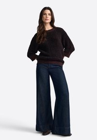 Maglione di lana marrone fuzzy con maniche ampie e orlo a coste, abbinato a jeans a gamba larga blu scuro con orlo risvoltato.