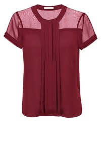 Blouse bordeaux avec manches courtes en maille, encolure ronde, plis sur le devant et détails de boutons. Fabriquée en tissu léger et transparent.