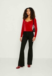 Haut en velours rouge à manches longues avec un décolleté en cœur, associé à un pantalon évasé noir et des chaussures rouges, complétant l'ensemble avec un petit sac noir.