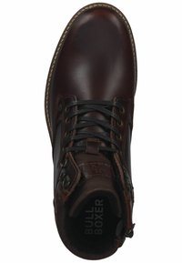Botín de cuero marrón hasta el tobillo con cordones negros, textura suave, acentos cosidos y puntera redonda. La etiqueta interior muestra "BULL BOXER."