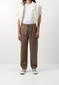 Beige bomulds cargo bukser med elastisk talje, multiple lommer og en afslappet pasform, parret med en hvid t-shirt og en cremet sweater.