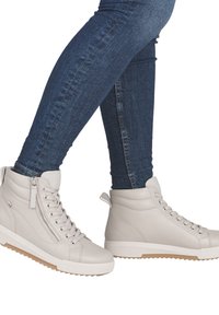 Baskets montantes gris clair en cuir texturé, avec lacets et fermeture éclair, semelle en caoutchouc et petit détail de marque. Portées avec un jean bleu foncé.