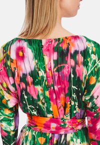 Mehrfarbiges Blumenkleid aus plissiertem Stoff; lebendige Farbtöne in Grün, Pink und Orange; mit einem orangen Taillengürtel und Knopfdetails.