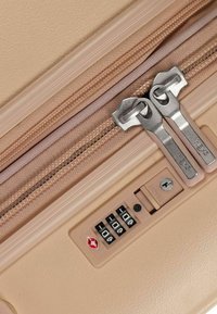 Valigia beige con zip a due vie e maniglie metalliche, serratura a combinazione e superficie texture. Dettagli in tonalità rosa morbido.