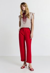 Top beige a maniche corte con bordi volanti, abbinato a pantaloni rossi a vita alta con pinces. Completato con mule rosse con tacco.