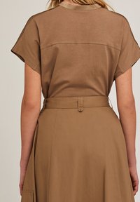 Blouse marron à manches courtes avec un col rond, associée à une jupe marron assortie avec une taille ceinturée et une coupe fluide.