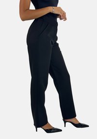 Zwarte op maat gemaakte broek met een hoge taille, voorvouwen en een gladde textuur. Gepaard met puntige zwarte hakken voor een strakke uitstraling.