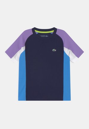 Sportowa koszulka z krótkim rękawem w blokach kolorów granatowego, fioletowego, białego i niebieskiego z logo krokodyla Lacoste na piersi.