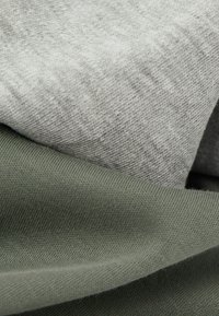Zwei Stoffmuster: eines in hellgrau mit einer dezenten Textur und eines in kräftigem Dunkelgrün mit einer gerippten Oberfläche. Beide sind weiche, gewebte Materialien.