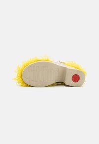 Gul fluffy sålesåle med en jevn beige fotbed, med merkevarenavnet "fitflop" preget inn og en rød sirkulær logo.