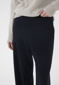 Navyblå, vidde bukser lavet af et glat stof med en høj talje og sidelommer. Toppen er lysegrå og strikket med tekstur.