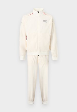 Bílá tepláková souprava na zip s vysokým límcem, elastickými manžetami, logem EA7 na hrudi a červenými prvky zipu na kapse bundy.