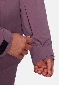 Lila langärmliges Shirt mit einem Reißverschlussdetail an der Manschette und einem Klettverschlussriemen. Der Stoff hat eine glatte, leicht glänzende Textur.