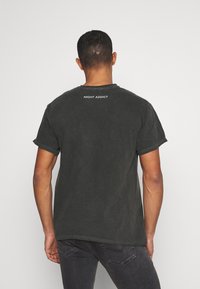 Černé bavlněné tričko s ohrnutými rukávy a kulatým výstřihem. Na zadní straně je v bílém natištěn nápis "NIGHT ADDICT" s kontrastním prošíváním.