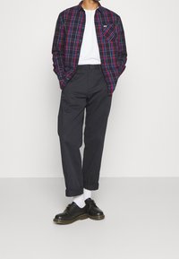 Koszula w kratę w kolorze granatowym, czerwonym i białym, zapinana na guziki, z kieszenią na piersi, zestawiona z ciemnymi spodniami wąsko dopasowanymi i czarnymi butami na grubej podeszwie.