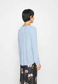 Chemisier bleu clair à manches longues avec un col rond et un pli au dos. Associé à une jupe noire à motif floral. Texture de tissu lisse.