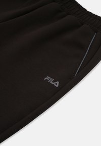 Svarta sweats med mjukt tyg, utrustade med ett elastiskt midjeband, sidOFICKOR och en reflekterande grå logotypdetalj på vänster ben.