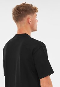 Czarny bawełniany t-shirt, krótki rękaw, okrągły dekolt. Widok z tyłu ukazuje gładką teksturę i luźny krój z czystymi detalami szycia.