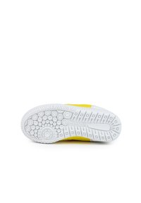 Zapatilla deportiva amarilla con una parte superior texturizada, suela de goma blanca con patrones de agarre circulares y rectangulares, y marca en la suela.
