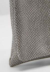 Gros plan d’un tissu gris texturé avec un motif hexagonal d’écailles, montrant les plis et les détails du matériau.