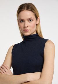 Top fără mâneci, de culoare bleumarin, dintr-un tricot moale, cu guler înalt și un croi ajustat care evidențiază umerii.