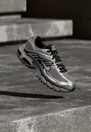 Nike Air Max futócipő ezüst, fekete és lila hálós anyagból, levegőben, betonfelület és lépcsők felett ábrázolva.