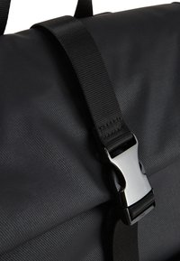 Schwarze Rolltop-Tasche mit strukturierter Oberfläche, ausgestattet mit einem Kunststoffschnallenriemen und glatten Akzenten, die ihr funktionales Design unterstreichen.