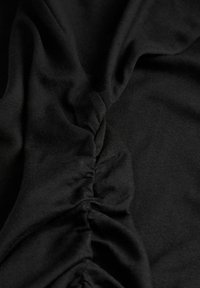 Μαύρο ύφασμα με κεντρική ραφή που δημιουργεί υφασμάτινες πτυχές και ζάρες, υπογραμμίζοντας το μαλακό και ελαστικό υλικό.