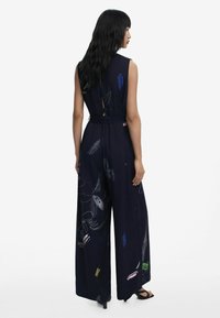 Navy jumpsuit with wide legs, sleeveless design, featuring colorful hand-drawn floral patterns. Includes a belted waist and open back detail.