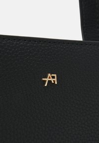 Sort lædertaske med en tekstureret overflade og et guldfarvet logoaccent. Designet inkluderer syningsdetaljer og en strømlinet silhuet.