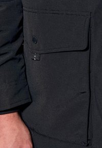 Materiale tessile nero con una grande tasca a patta, bottone rotondo e dettagli cuciti, che mostra una texture liscia.