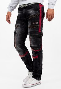 Pantalons cargo en denim noir avec des accents rouges, plusieurs poches zippées et une coupe ajustée. Présente un tissu texturé et des détails imitant le cuir.