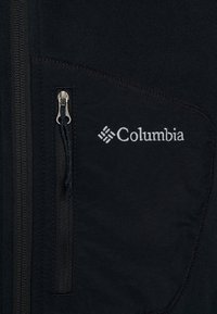 Čierna fleecová bunda s vreckom na zips, prešívanými akcentami a vyšitým logom Columbia na prsiach. Mäkká textúra a priliehavý strih.