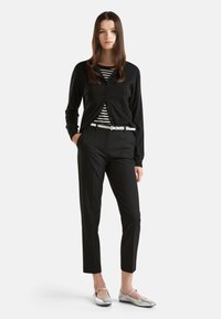 Zwarte cardigan over een gestreept shirt, gecombineerd met zwarte broek en zilveren ballerina's. Gestructureerde materialen en een slim fit ontwerp zijn zichtbaar.