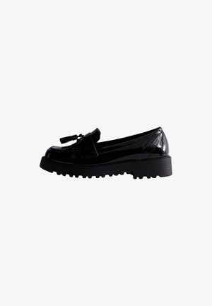 Mocassins en cuir verni noir avec une semelle épaisse, ornés d'un pompon décoratif et d'une couture contrastée le long du bord supérieur.