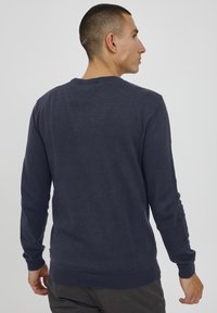 Dunkelblau gestrickter Pullover mit langen Ärmeln, gerippten Bündchen und Saum. Glatte Textur, Rundhalsausschnitt und minimale Details auf der Rückseite.
