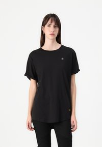Black oversized t-shirt made from cotton. Short rolled sleeves, round neckline, small logo detail on chest, falls to hips. Classic cut.