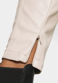Stivale alla caviglia in pelle crema con dettaglio della cerniera laterale, caratterizzato da un bordo in tessuto nero testurizzato alla base. Finitura liscia e design aderente.