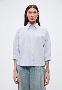 Ανοιχτό μπλε πουκάμισο με κουμπιά και γιακά, με μανίκια τριών τετάρτων, άνετη εφαρμογή και διακριτικές λεπτομέρειες ραφής.