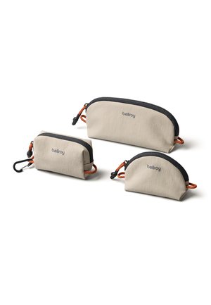 Tre pochette Bellroy beige di dimensioni diverse con cerniere nere e cordini arancioni su uno sfondo bianco.