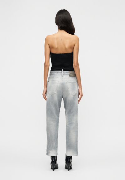 Ανοιχτό γκρι τζιν με άνετη εφαρμογή, σχέδιο με πέντε τσέπες και διακριτικές φθορές, συνδυασμένο με μαύρο τοπ χωρίς τιράντες και μαύρες ψηλοτάκουνες παπούτσια.