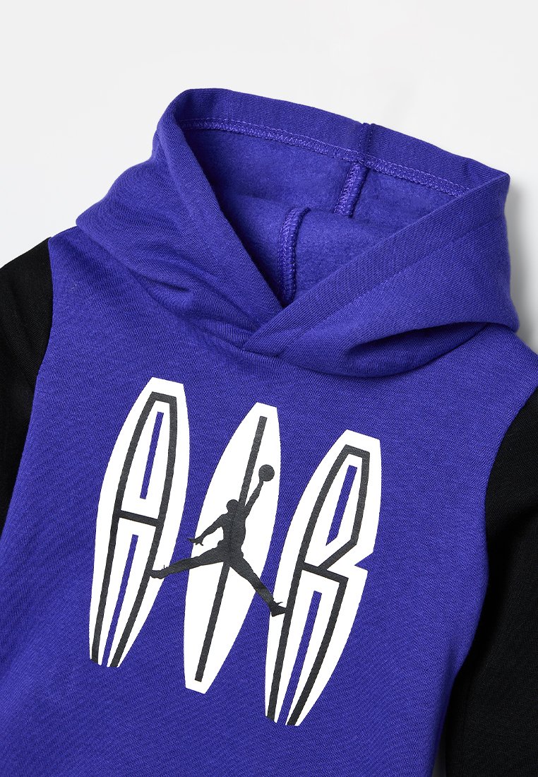 Sudadera morada con mangas negras. Presenta un gráfico de una silueta saltando y las letras "A AIR" en blanco. Textura de mezcla de algodón.
