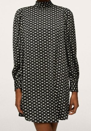 Robe courte noire à manches longues avec motif géométrique blanc en losange, col montant et épaules légèrement bouffantes portée par une personne debout.