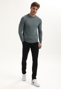 Vaalean teal-välinen neulepaita, jossa on pyöreä pääntie, kapea malli ja ribattu helma; yhdistetty mustiin kapeisiin housuihin ja valkoisiin tennareihin mustilla yksityiskohdilla.