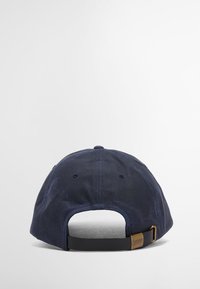 Boné de beisebol em algodão azul-marinho escuro com coroa arredondada, faixa ajustável preta e ferragens em latão. Tecido texturizado com detalhes de costura sutis.