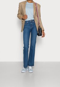 Beige liinakund, helesinine T-särk, laiad sinised teksapüksid ja helesinised tossud. Väike must käekott triibulise rihmaga.