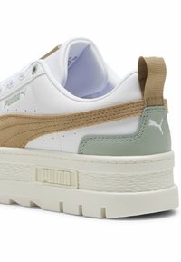 Vit sneaker med tan mocka och mintgröna accenter. Har en texturerad sula och vadderad krage, med en framträdande varumärkeslogotyp.