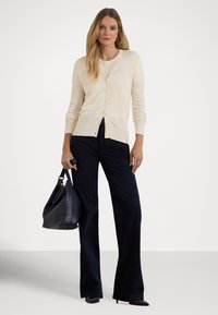 Svetlobéžový kardigán s textúrovaným vzorom a zapínaním na gombíky vpredu, doplnený tmavomodrými širokými nohavicami. Tmavá kabelka dokončuje celý vzhľad.