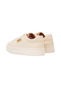 Sneaker di colore crema con parte superiore in pelle liscia, punta rotonda e suola spessa e texturizzata. Presenta una placca con il logo in tono oro sul lato.