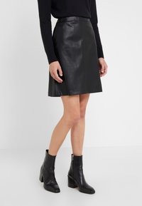 Musta nahkainen A-linjainen hame, jossa on sileä pinta, kapea vyötärö ja polven mittainen malli, yhdistetty mustiin nilkkureihin, joissa on vetoketju.